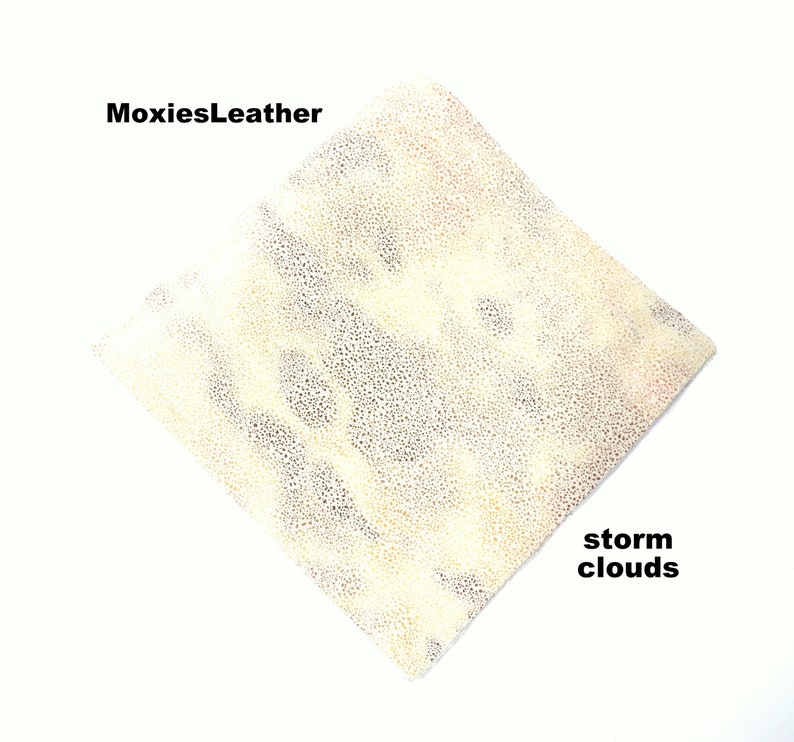 Puede incluir: Primer plano de un trozo de cuero blanco roto con una superficie texturizada. El cuero tiene un patr&oacute;n sutil de peque&ntilde;os puntos oscuros. El texto "MoxiesLeather" aparece en la esquina superior izquierda de la imagen. El texto "storm clouds" aparece en la esquina inferior derecha de la imagen.