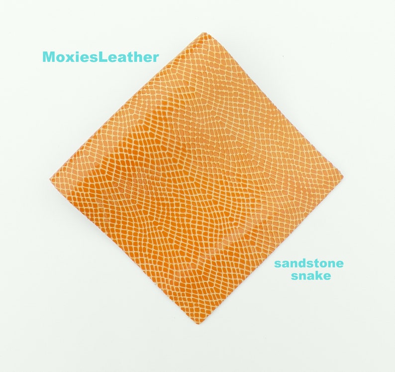 May include: A square piece of sandstone snake embossed leather in a light orange colour. The leather is textured with a snake skin pattern.