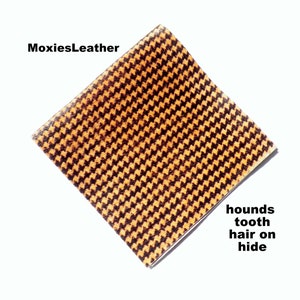 May include: A close-up of a piece of brown and yellow houndstooth patterned leather. The leather has a textured surface and is called "hounds tooth hair on hide".