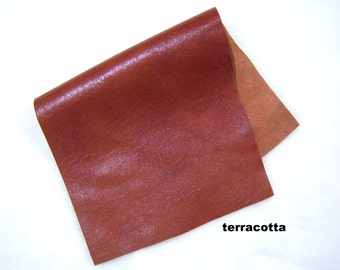 May include: A piece of terracotta leather with a smooth, shiny finish. The leather is folded in half, revealing the underside.