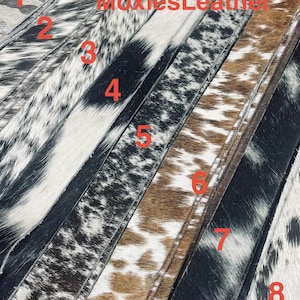 May include: A selection of leather strips with diverse cowhide patterns. The strips showcase a variety of colours, including black, white, brown, and grey. The text "MoxiesLeather" is visible in red across the image.