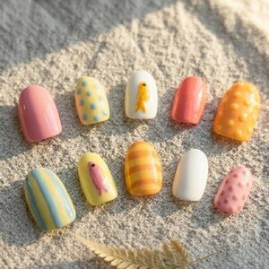 May include: A set of ten press-on nails featuring various designs including solid pink, yellow with blue dots, white with a yellow fish, solid coral, orange with raised dots, blue and yellow stripes, yellow with a pink fish, orange stripes, solid white, and pink dots.