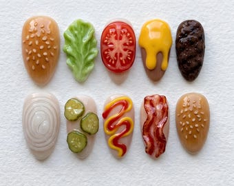 May include: A set of ten acrylic nails designed to resemble the components of a hamburger. The nails feature detailed depictions of a sesame seed bun, lettuce, tomato, cheese, a burger patty, onion, pickles, mustard, and bacon.