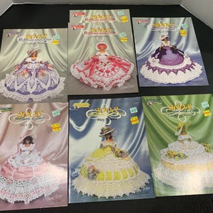 May include: A collection of six magazines featuring doll dresses. Each cover showcases a doll in a crocheted dress, with varying colors like pink, purple, yellow, and white. The magazines are titled "2003 Ribbons and Lace".