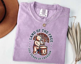 Camiseta "Land Of The Free Comfort Colors" | Camiseta retrô com caixa de bateria e urso colonial | Camiseta comemorativa do 250º aniversário dos EUA | Presente para o 4 de julho de 2026