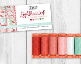 May include: A set of seven spools of thread in shades of red, pink, white, green, and brown. The spools are labeled "Aurifil" and "Lighthearted by Camille Roskelley". The text "Wherever you go, go with all your heart" is also visible on the packaging.