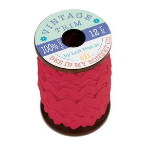 May include: A spool of red vintage trim with a scalloped edge. The spool is labeled "Vintage Trim" and "12 yds" with the text "Bee in My Bonnet Co." and "100%" on the label. The trim is wound around a wooden spool.