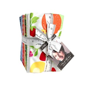 May include: A stack of colorful fabric squares tied with a white ribbon printed with measurements. The fabric features a strawberry and fruit pattern on a white background. A tag with a woman's photo and the words "moda FABRICS + SUPPLIES" is attached.