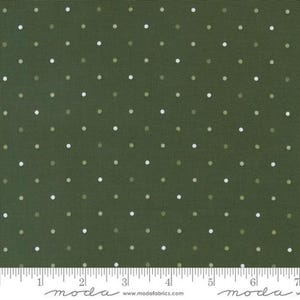 May include: Close-up of a fabric with a dark olive green background and a repeating pattern of small, evenly spaced white and light green dots. The fabric has a textured appearance. A ruler is at the bottom.