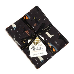 May include: A bundle of eight fat quarter fabric squares featuring a spooky Halloween theme with a black background and colorful illustrations of ghosts, witches, and other Halloween characters. The fabric bundle is tied with black ribbon and includes a label that reads "Good Spirits Collaborative Collection Fat Quarter Bundle".