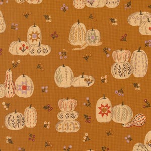May include: A mustard yellow fabric featuring a repeating pattern of cream-colored pumpkins and gourds. The pumpkins are decorated with various geometric shapes, star motifs, and botanical line drawings, interspersed with small clusters of tiny flowers.