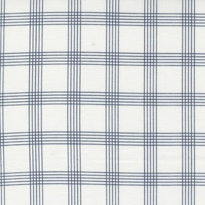 May include: White fabric with a navy blue plaid pattern. The grid design features evenly spaced vertical and horizontal lines, creating a classic and versatile textile design. The fabric appears to be a medium weight, suitable for various sewing projects.