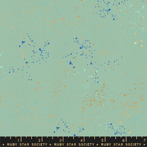 May include: A light green fabric with a speckled pattern of blue and gold dots. The fabric has a ruler printed on the bottom with the text "Ruby Star Society" repeated.