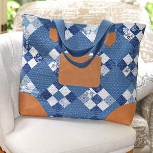 May include: A blue patchwork tote bag with a geometric pattern of squares and diamonds. The bag has brown leather accents on the corners and a large brown leather pocket. The handles are a solid blue color.