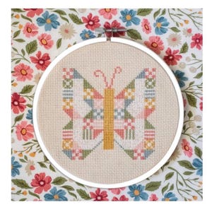 May include: A cross-stitch butterfly design in a white hoop. The butterfly features a geometric pattern in pastel pink, blue, green, and yellow. The background is a floral fabric with red, pink, and blue flowers.