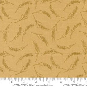 May include: A beige fabric with a repeating pattern of wheat stalks in a brown color. The fabric has a subtle linen texture. The fabric is marked with a ruler in inches and the words "moda" and "www.modafabrics.com".