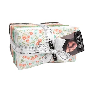May include: A stack of 12 fabric squares with a floral print in shades of white, green, and peach. The fabric is tied together with a white ribbon and a measuring tape. The label reads "Moda Fabrics - Supplies".