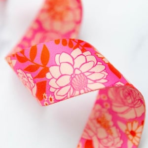 May include: A length of grosgrain ribbon featuring a vibrant hot pink background with a repeating floral pattern in shades of light peach and bright orange. The design includes stylized blossoms, leaves, and small circular accents throughout.