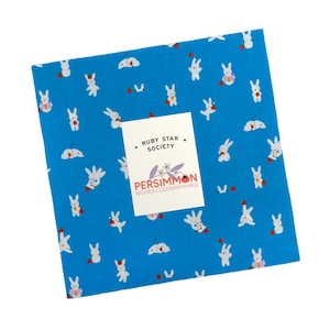 May include: Square fabric piece with a vibrant blue background, adorned with white rabbits and small red accents. A white label displays "RUBY STAR SOCIETY" and "PERSIMMON" text. The fabric is likely for quilting or crafting.