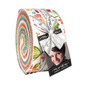 May include: A rolled bundle of fabric strips, featuring a colorful array of rainbow hues. The fabric is tied with a white ribbon and a tag with the text "moda FABRICS + SUPPLIES". The fabric roll is decorated with floral patterns.