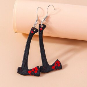 May include: A pair of black axe-shaped earrings with red splatter details. The earrings have silver-colored fish hook ear wires. The axes are a novelty item.