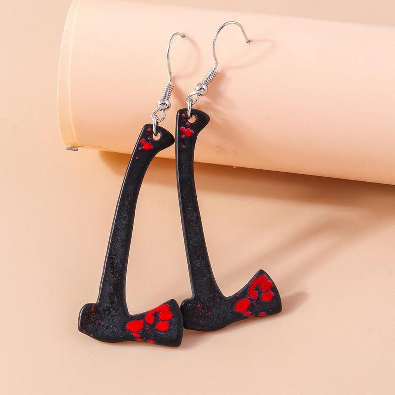 May include: A pair of black axe-shaped earrings with red splatter details. The earrings have silver-colored fish hook ear wires. The axes are a novelty item.
