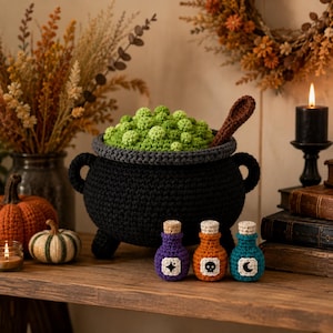 May include: A black crocheted cauldron filled with green textured spheres and a brown spoon, accompanied by three small crocheted potion bottles in purple, orange, and teal, each featuring a white label with a star, skull, or moon icon.