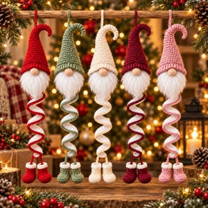 May include: Five hanging crochet gnome ornaments in a row, each featuring a tall pointed hat, a round beige nose, a white faux fur beard, and a long spiraling body ending in two small matching boots. The gnomes are red, sage green, cream, burgundy, and pink.