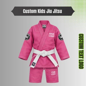May include: A pink martial arts gi for children featuring a white belt, long sleeves, and a wrap-around jacket design. The garment includes text that reads Custom Kids Jiu Jitsu, Your Logo, and Custom Text Logo, with circular crown emblems.