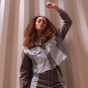 Könnte beinhalten: Eine Jeansjacke im Patchwork-Design. Die Jacke hat eine Mischung aus grauen, hellblauen und braunen Stoffbahnen und einen rohen Saum. Die Person trägt die Jacke mit einer passenden Hose.