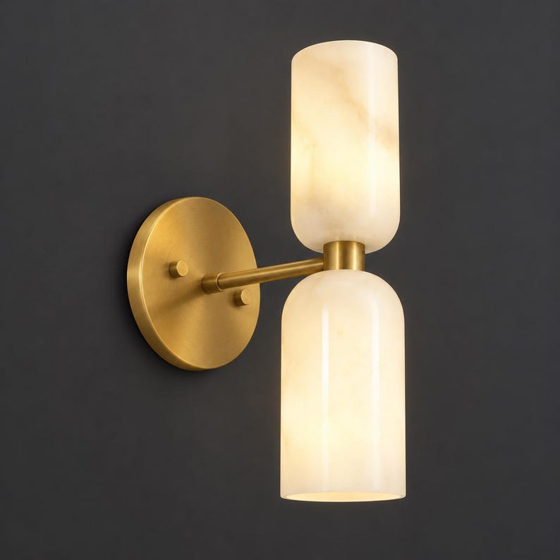 May include: A wall sconce featuring a circular brushed brass backplate and a horizontal arm extending to two vertically stacked, cylindrical, translucent white stone shades that emit a soft, warm glow from within the light fixture.