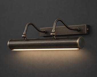 Pode incluir: Uma luminária para quadros em bronze escuro com uma placa de montagem retangular, dois braços curvos ajustáveis e uma cabeça cilíndrica que emite uma luz quente direcionada para baixo ao longo de todo o seu comprimento.