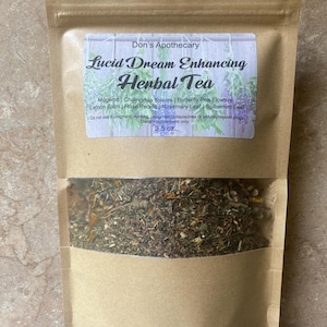 Pode incluir: Um saco de papel castanho com uma janela transparente, cheio de ervas secas. O rótulo diz "Lucid Dream Enhancing Herbal Tea" da Don's Apothecary. Contém artemísia, flores de camomila e flores de ervilha borboleta. O saco contém 99 gramas de chá.