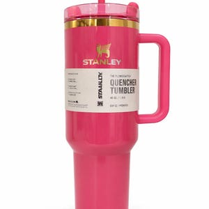 K&ouml;nnte beinhalten: Ein leuchtend pinkfarbener Stanley Quencher Tumbler mit Griff und transparentem Deckel. Der Becher hat einen goldenen Rand und das Stanley-Logo. Das Etikett lautet "Quencher Tumbler 40 oz / 1.18L".