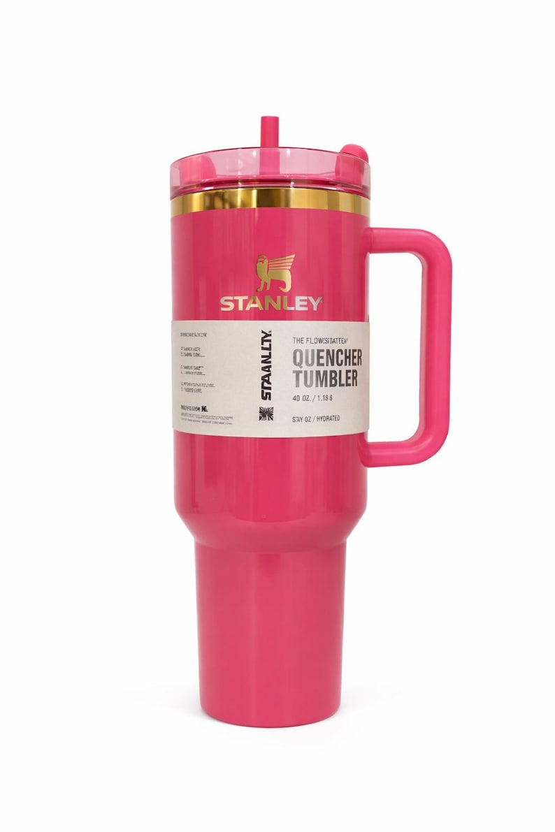 K&ouml;nnte beinhalten: Ein leuchtend pinkfarbener Stanley Quencher Tumbler mit Griff und transparentem Deckel. Der Becher hat einen goldenen Rand und das Stanley-Logo. Das Etikett lautet "Quencher Tumbler 40 oz / 1.18L".