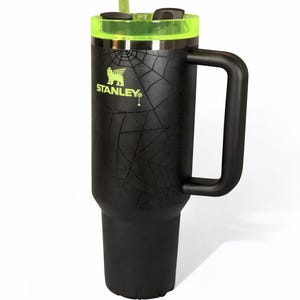 May include: Black Stanley tumbler with a neon green lid and straw. The tumbler has a handle and a spiderweb design. The Stanley logo is visible on the side.