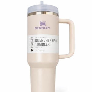 Puede incluir: Vaso Stanley Quencher H2.0 de color crema con asa y tapa transparente. El vaso tiene el logotipo de Stanley y el texto "QUENCHER H2.0 TUMBLER" impreso. Contiene 1,18L. El texto "STAY HYDRATED" tambi&eacute;n est&aacute; impreso en el vaso.