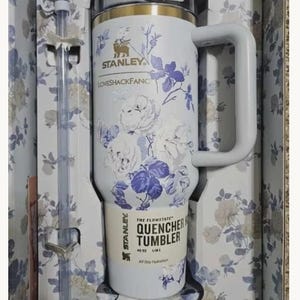 May include: A white Stanley Quencher H2.0 Flowstate tumbler with a 40 oz capacity, featuring a blue floral pattern, a gold rim, and a matching handle. The tumbler includes a clear straw with a white bow topper, all packaged in a floral box.