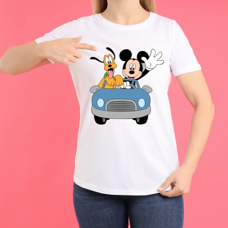 Op de afbeelding: Wit T-shirt met een cartoon illustratie van Mickey Mouse en Pluto in een blauwe auto. Mickey Mouse zwaait en Pluto steekt zijn tong uit. Het ontwerp staat in het midden van het shirt.