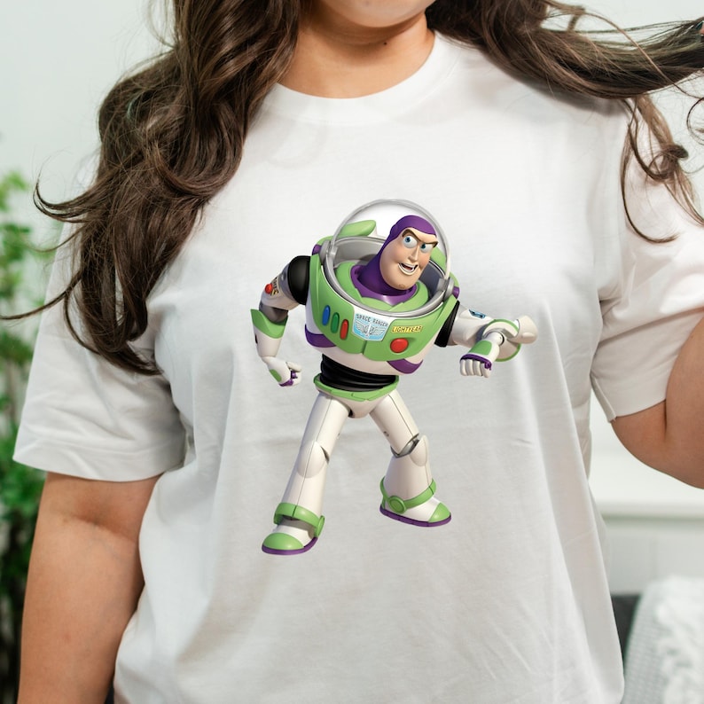 May include: White t-shirt featuring a colorful graphic of Buzz Lightyear from Toy Story. The character is depicted in his signature green, white, purple, and black spacesuit, with a determined expression. The design is centered on the shirt.