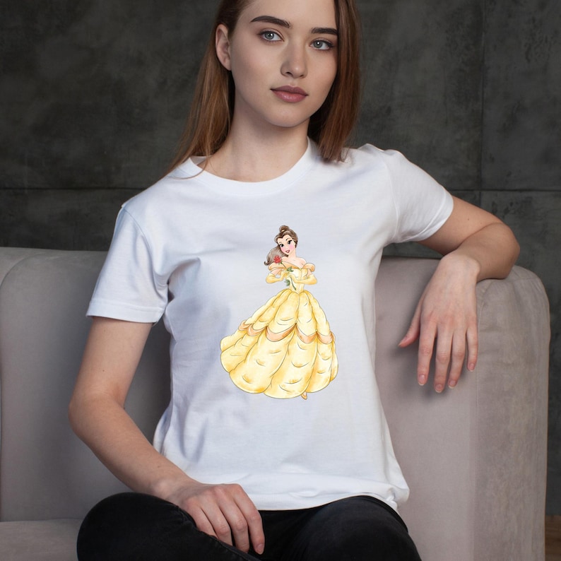 May include: White t-shirt featuring a watercolor illustration of a princess in a yellow gown holding a red rose. The princess has brown hair and is wearing a yellow dress with gold accents. The t-shirt is a classic crew neck style.