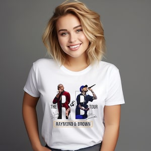 May include: White t-shirt featuring a graphic of two performers with the text "THE R & B TOUR" and "RAYMOND & BROWN". One performer is wearing a red jacket, and the other is wearing a blue cap and black shirt.