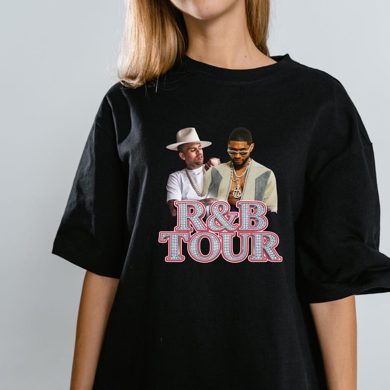 May include: Black t-shirt featuring a graphic of two men with the text "R&B TOUR" in a sparkling, gem-like font. The image shows the men in front of a light background. The t-shirt is a classic crew neck style.