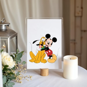 Op de afbeelding: Een ingelijste print met Mickey Mouse die Pluto omhelst. Mickey draagt zijn kenmerkende rode broek en gele schoenen. Pluto is een gele hond met een groene halsband. De print staat op een houten standaard.