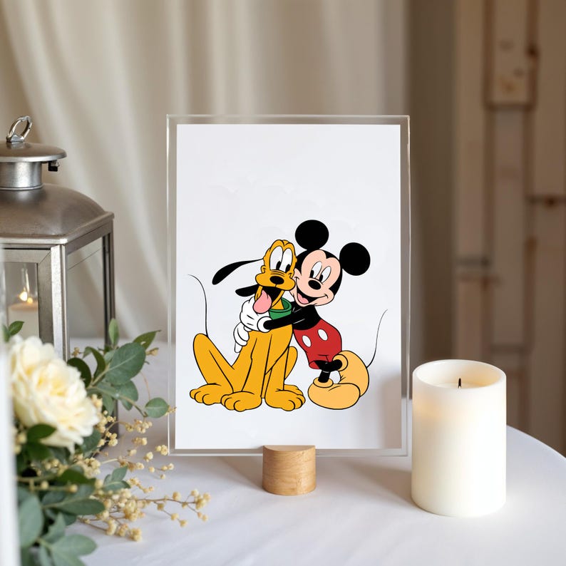 Op de afbeelding: Een ingelijste print met Mickey Mouse die Pluto omhelst. Mickey draagt zijn kenmerkende rode broek en gele schoenen. Pluto is een gele hond met een groene halsband. De print staat op een houten standaard.