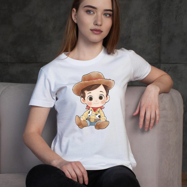 May include: White t-shirt featuring a cartoon illustration of a cowboy character. The cowboy is wearing a brown hat, a yellow shirt with black spots, blue jeans, and a red bandana. The design is centered on the shirt.