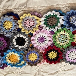 May include: A crocheted blanket made of colorful flower-shaped squares. The blanket is made of various colors, including blue, green, purple, yellow, and red.