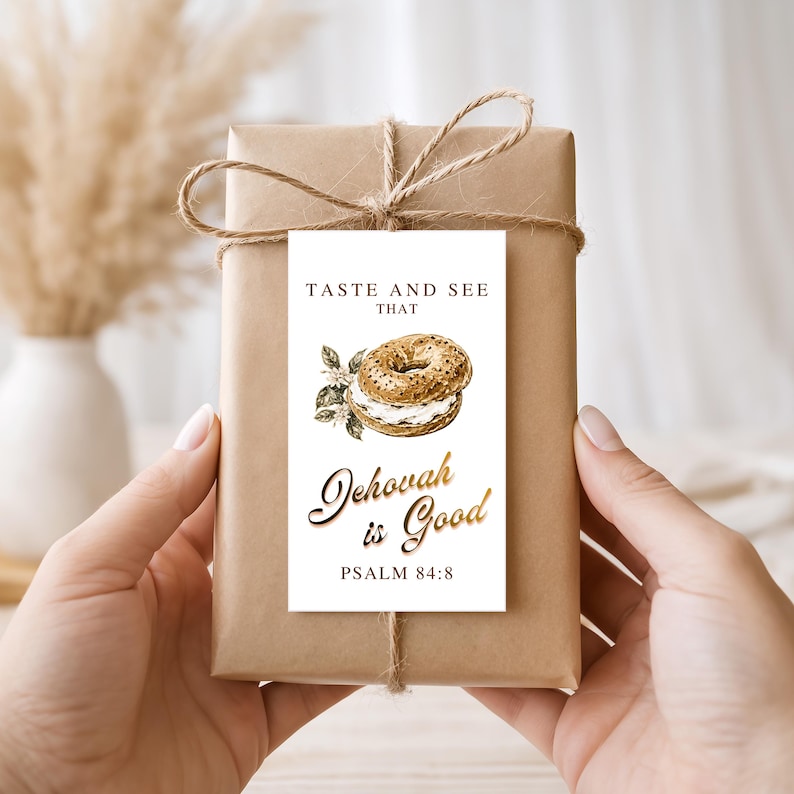 May include: A rectangular white gift tag tied with brown twine to a brown paper-wrapped package. The tag features a bagel illustration, the text TASTE AND SEE THAT, the gold-colored text Jehovah is Good, and the scripture reference PSALM 84:8.