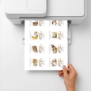 May include: A white sheet of paper emerging from a printer, featuring eight rectangular labels with watercolor illustrations of food and beverages. Each label includes the text "TASTE AND SEE THAT Jehovah is Good PSALM 34:8" in black script.