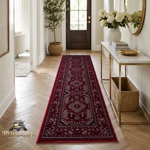 May include: A long, rectangular runner rug featuring a deep red base colour with intricate, symmetrical patterns in black, white, and subtle blue tones. The rug displays a traditional geometric border and a central medallion design motif.